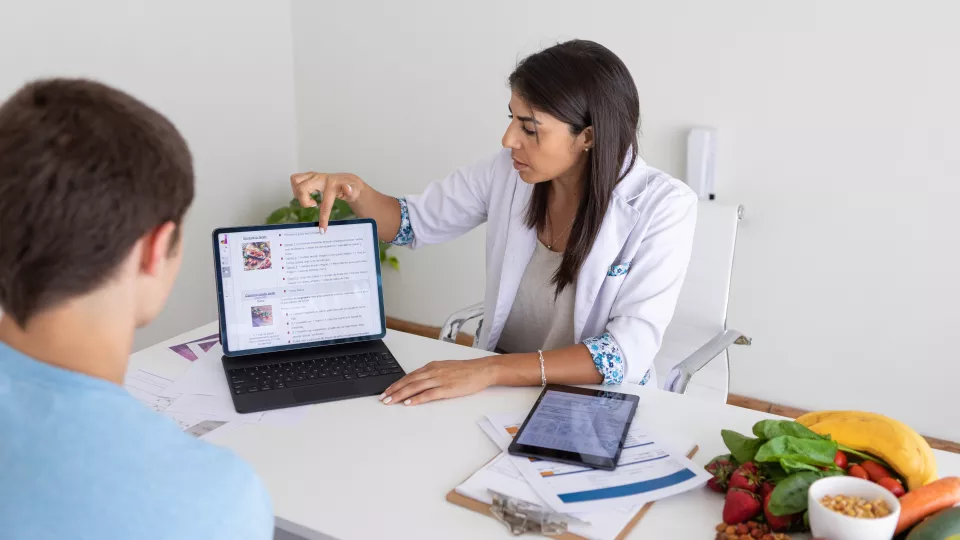 A medium skin-toned woman in a lab coat shows information on a laptop to a boy.