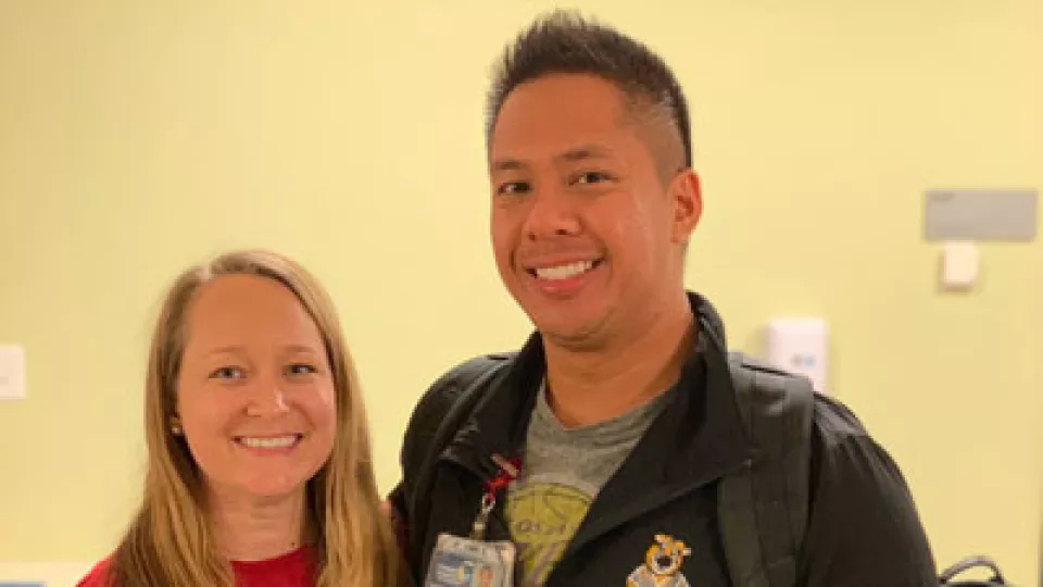 Smiling female nurse with light skin tone and long blonde hair stands with smiling male nurse with medium skin tone and short dark hair