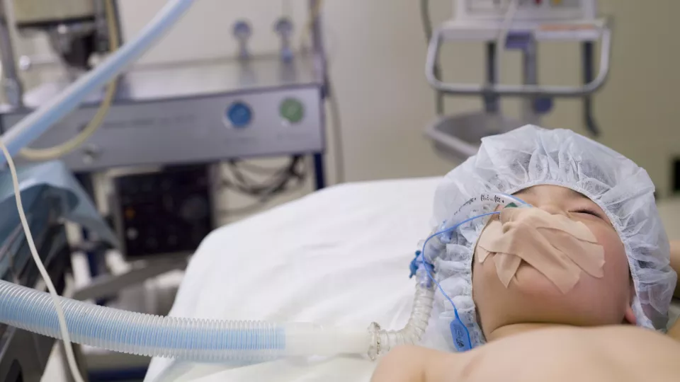 Young boy with medium skin tone and an anesthetic mask over his mouth lies on a hospital operating table