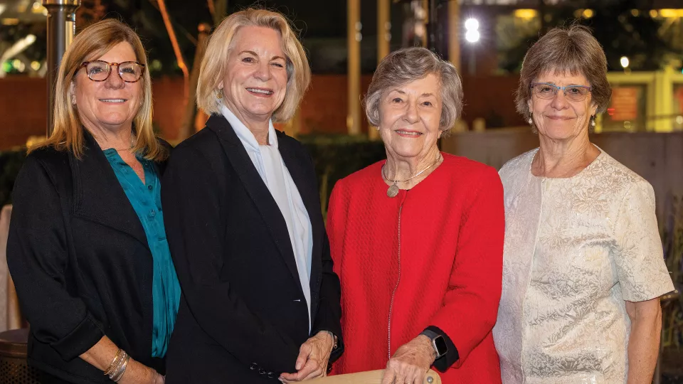 Four women with light skin tone and dressed in business attire smile for the camera