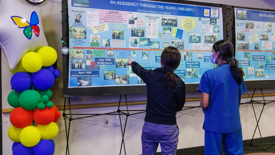 Two nurses look at a poster timeline of the RN Residency through the years.