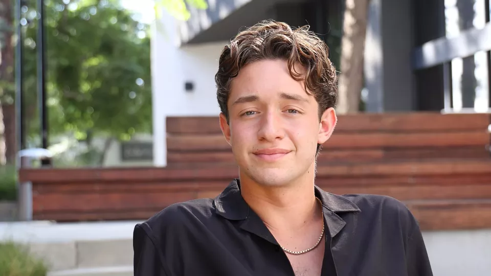 17-year-old Hunter sits in an outdoor courtyard wearing a black button down shirt.
