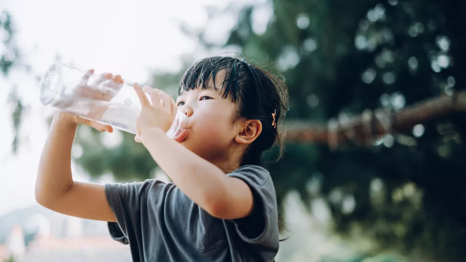 A child with medium light skin tone drinking from a large plastic water bottle.