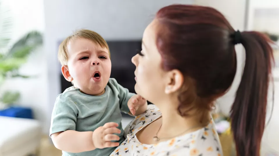 Light-skinned baby coughing in arms of light-skinned woman with brown hair