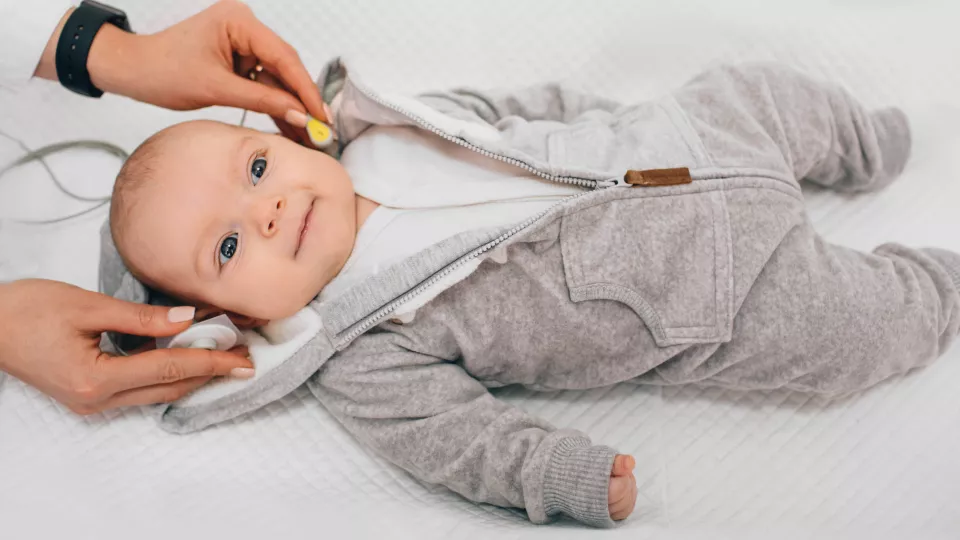 Infant in gray onesie receiving hear test