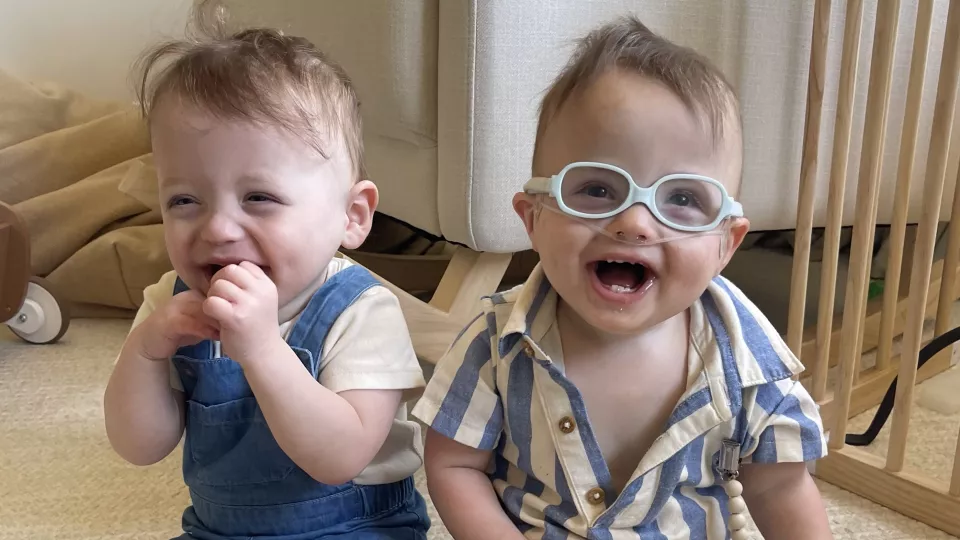 Two light-skinned toddlers seated beside each other, one wearing thick white glasses