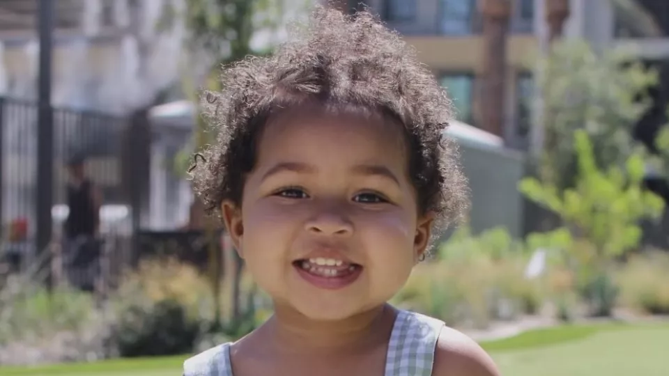 Toddler with light brown skin and dark hair smiling