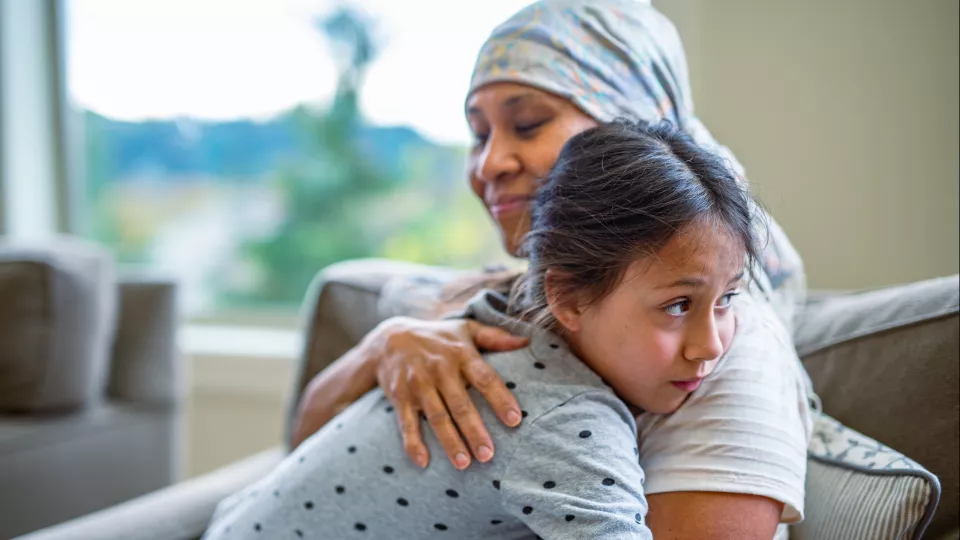 A young girl hugs her caregiver who wears a head scarf for cancer treatment. 