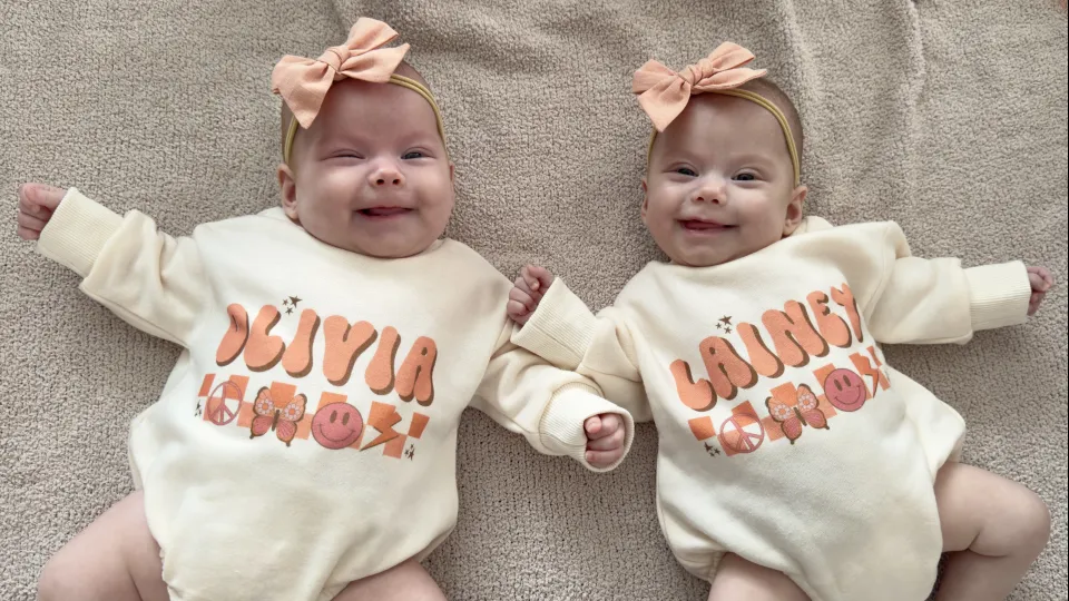 Twins lying beside each other wearing matching onesies with their names on them