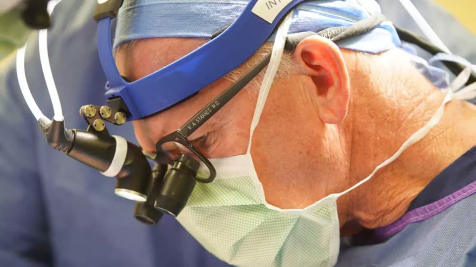 A male surgeon wearing a surgical mask, glasses and surgical magnifying lenses performs a surgical procedure