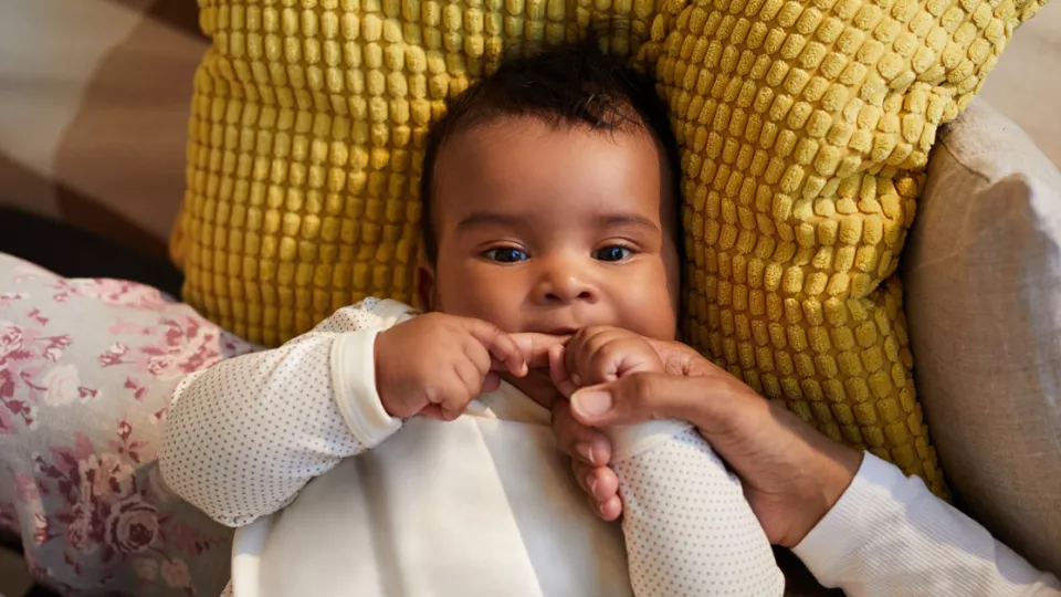 Baby holding and nibbling on parent's hand to relieve teething