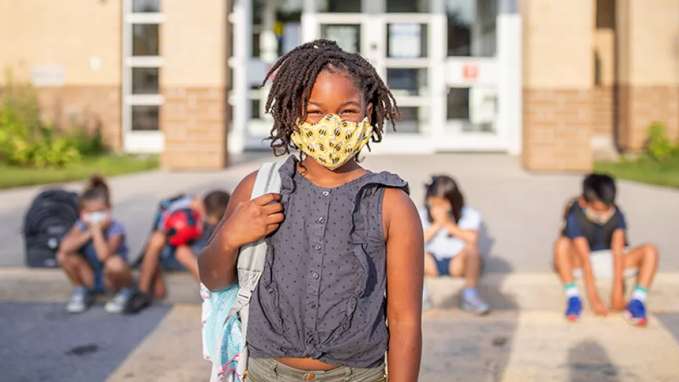 Young girl wearing face mask in front of school
