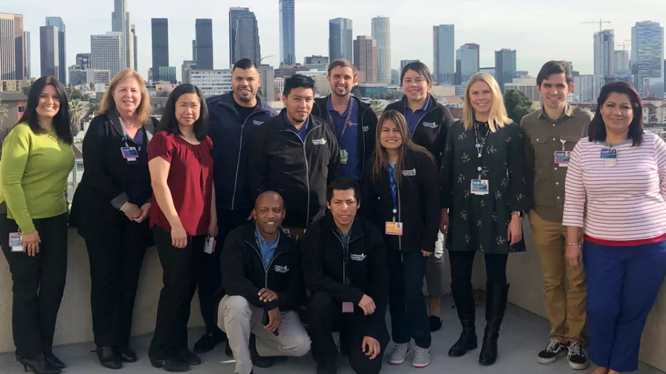 Group photo of participants of the CHLA Opening Doors to the World Project standing on the roof of CHLA with the downtown Los Angeles skyline in the background.