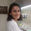 Headshot of a smiling young woman with medium skin tone and shoulder-length dark hair wearing a white lab coat in laboratory setting