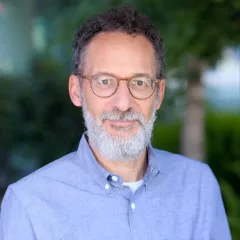 Michael Goran, a light skin toned man with a beard and glasses, against a background of green foliage