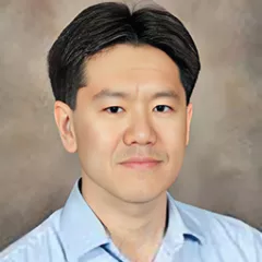 Headshot of a man with medium skin tone and short dark hair wearing a blue open-collar dress shirt against a neutral indoor background