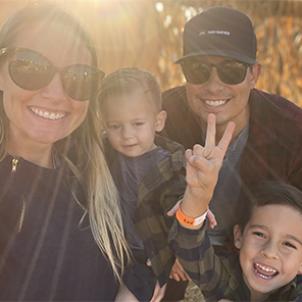 Family photo of Melinda, Kai, Chasen and Cruz smiling in the afternoon sun in an outdoor pumpkin patch