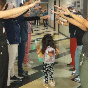 A little girl wearing a backpack walks down a hospital corridor between two rows of health care providers cheering her on