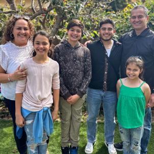 A smiling mother and father with medium skin tone pose for the camera with their four children