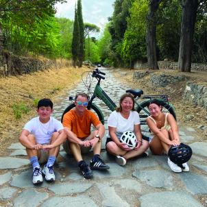 Family of four sit in front of bicycle on paving stone road
