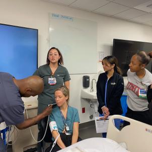 Nurse trainees practice taking patient's vital signs in a hospital room