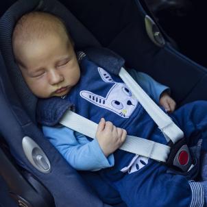 Infant in blue clothes sitting in car seat with 3-point harness and holding strap