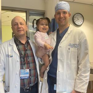 Baby held up by doctor on one side, with another doctor on her other side