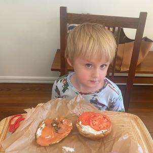 A young boy enjoys a lox bagel at home.