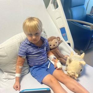 A young boy sits in a hospital bed surrounded by his favorite stuffed animals.
