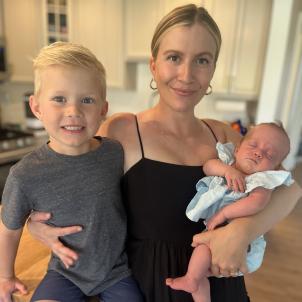 Woman with light skin and blond hair wearing black dress has an arm wrapped around each of two children