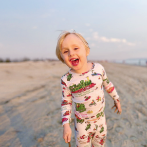 A young boy smiles while walking on a beach at sunset.