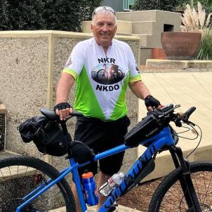 Older man with gray hair and smiling standing beside his bike