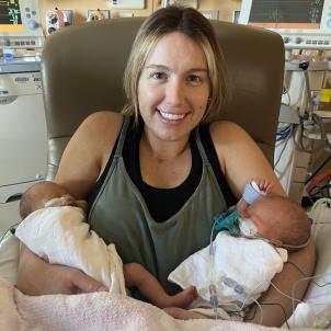 Smiling woman with light hair and light skin holding a baby in each arm