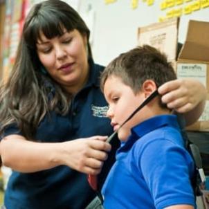 A light skin-toned woman adjusts a safety belt strap on a medium-light skin-toned boy