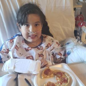 Xitlali smiling and eating in hospital bed, wearing a nasal canula
