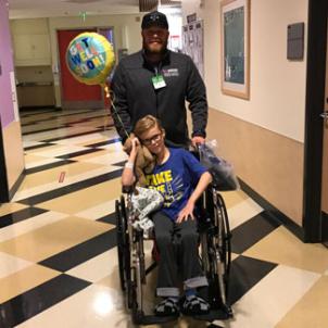 Malakai on a wheelchair being pushed by his father through the halls of CHLA