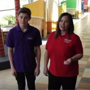 A light skin-toned teen boy stands next to a medium-light skin toned woman in a colorful hospital lobby. Both wear shirts with the CHLA logo.