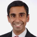 Headshot of smiling man with medium skin tone and dark hair wearing business attire against a white background