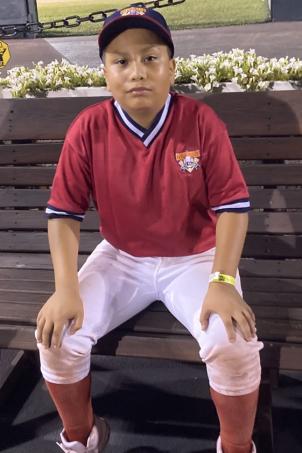 Teenage boy seated on bench wearing baseball cap, baseball jersey, baseball pants