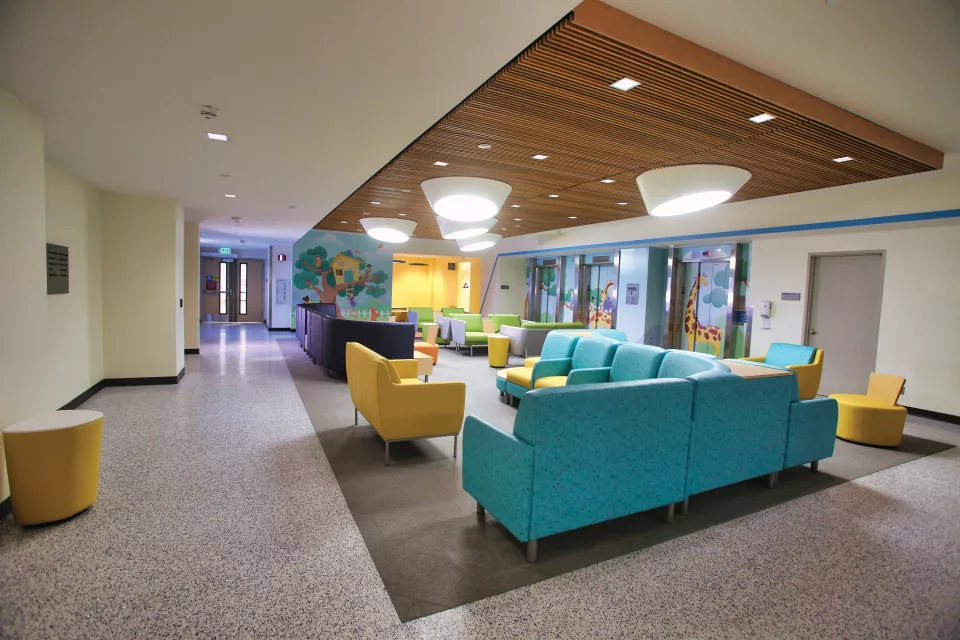 A colorful waiting room with teal and yellow furniture, playful wall art and bright lights.