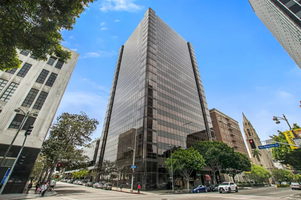A street-level view of a tall, glass-covered building on a tree-lined urban street