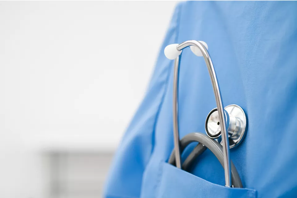 A stethoscope tucked into the breast pocket of blue medical scrubs.