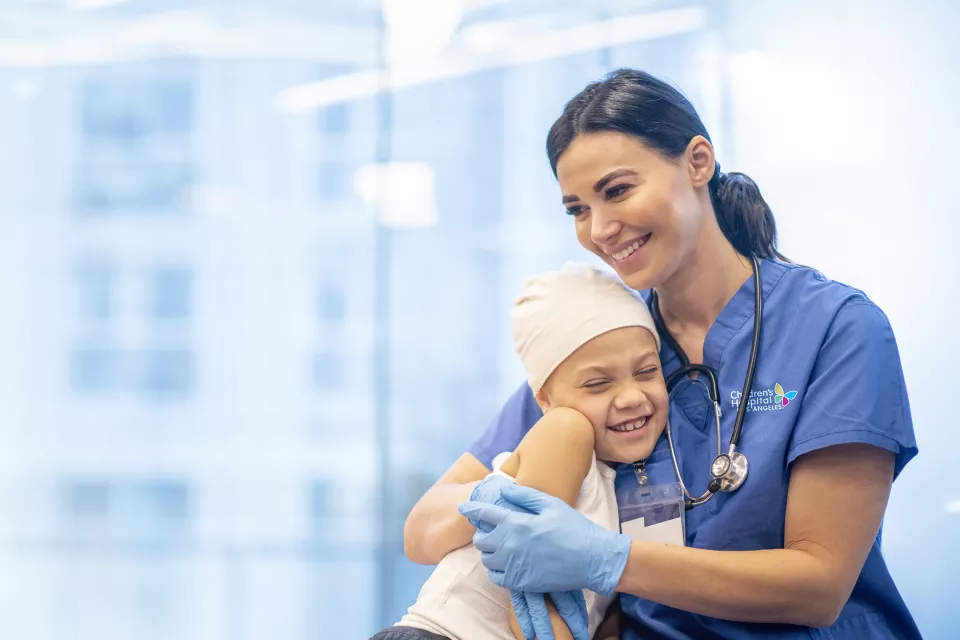 Nurse in blue scrubs hugging a child patient.