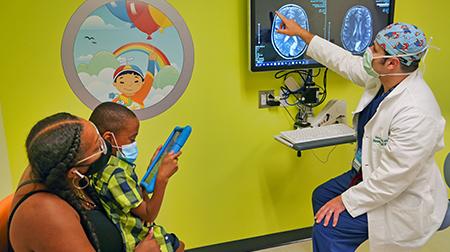 Physician explaining brain scans to mother while son plays with tablet