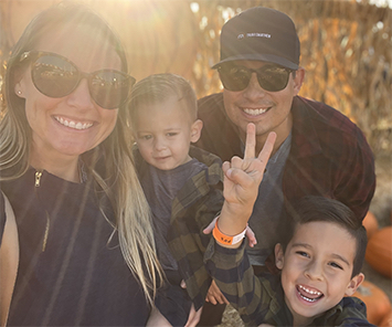 Family photo of Melinda, Kai, Chasen and Cruz smiling in the afternoon sun in an outdoor pumpkin patch