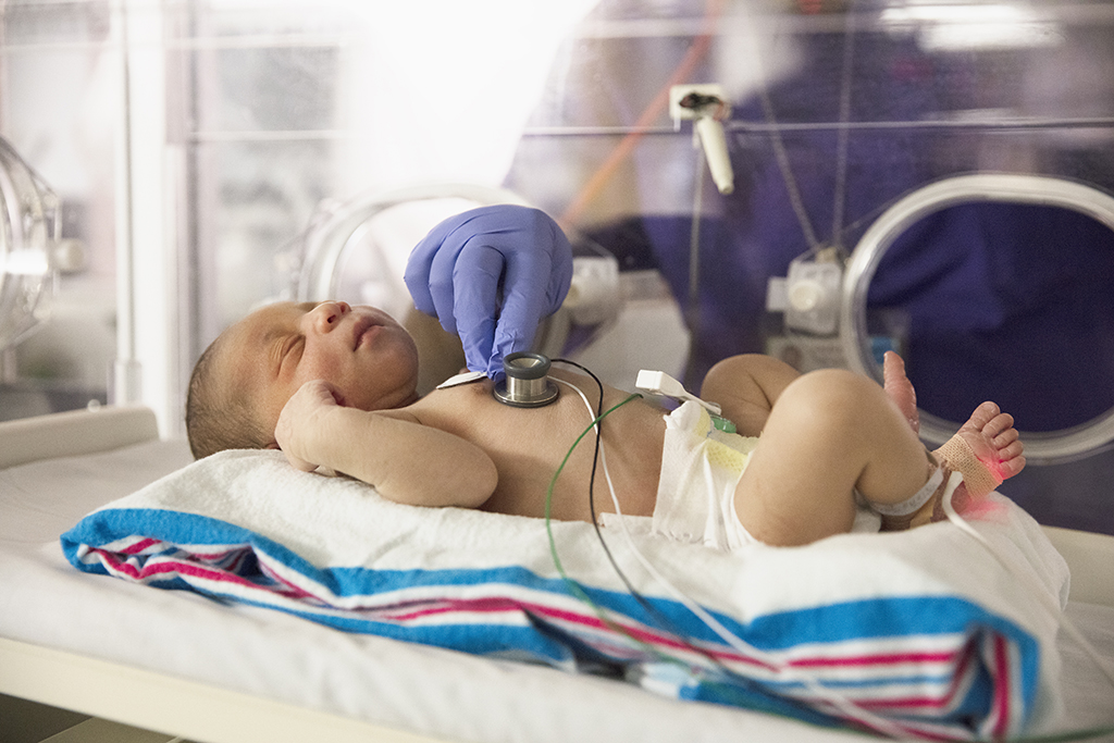 Health care professional places stethoscope on chest of infant that is resting in NICU isolette