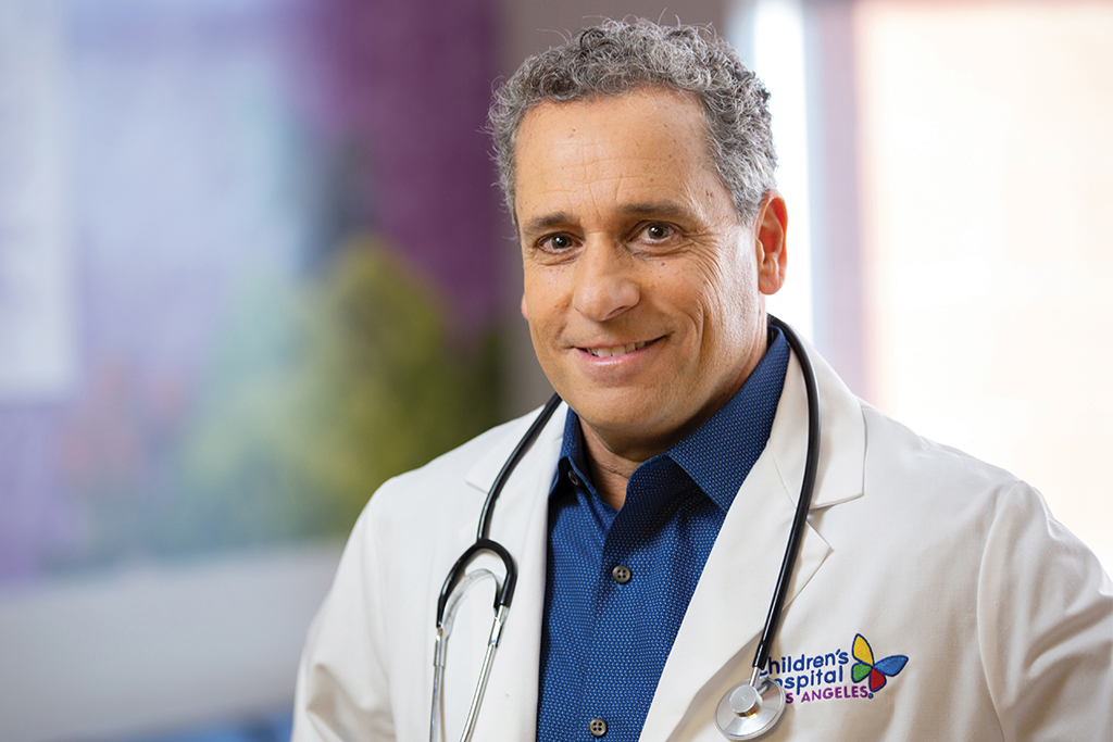 Guy Young, MD smiles in his lab coat with stethoscope draped around his neck
