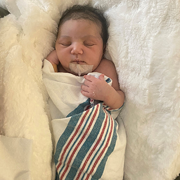 Ciara, a medium skin-toned infant, sleeps swaddled in a hospital blanket