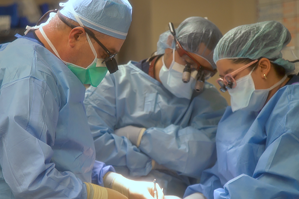 Three masked surgeons operate on a patient in a hospital operating room