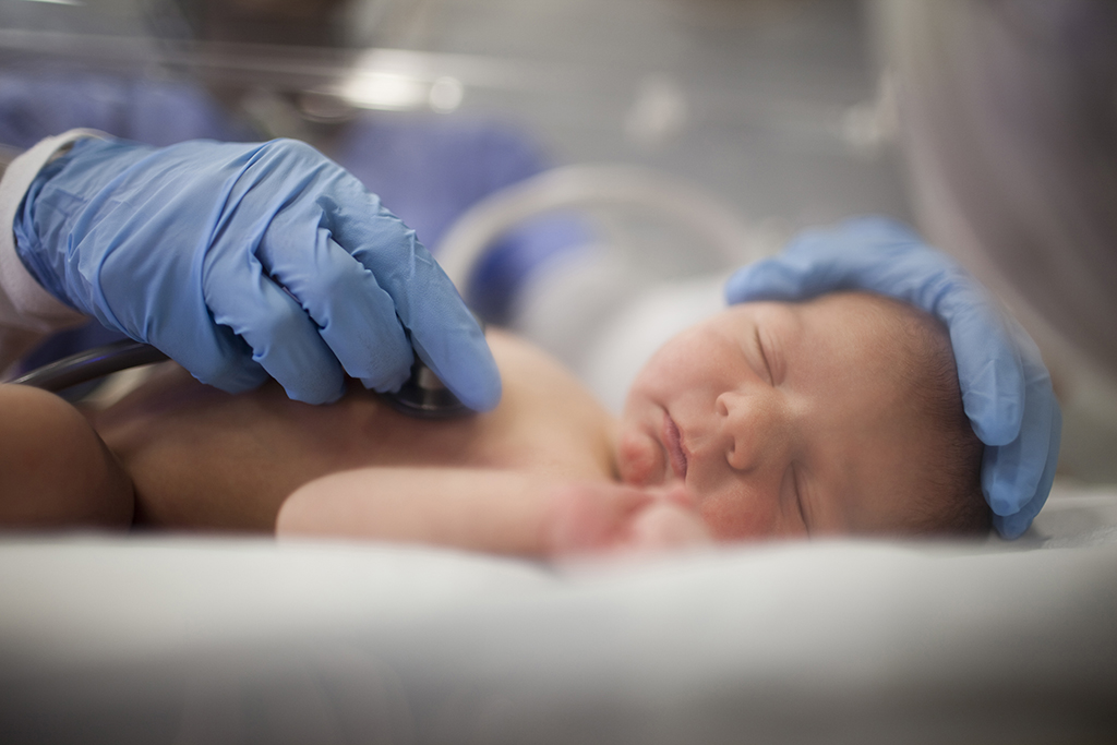 Nurse listens to heartbeat of newborn in incubator